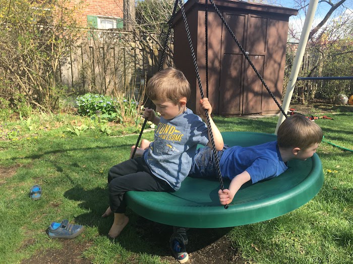 two boys on a spinning disc on a swing set in a backyard