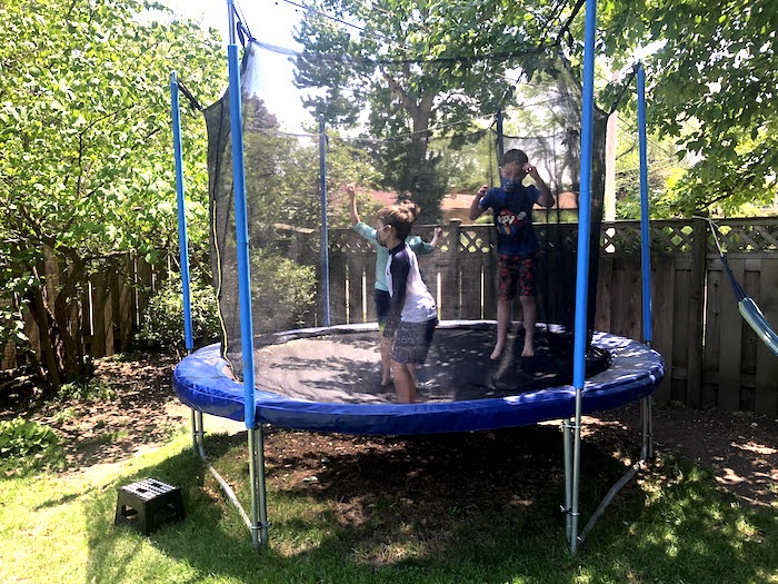 three boys jumping in a trampoline in a backyard