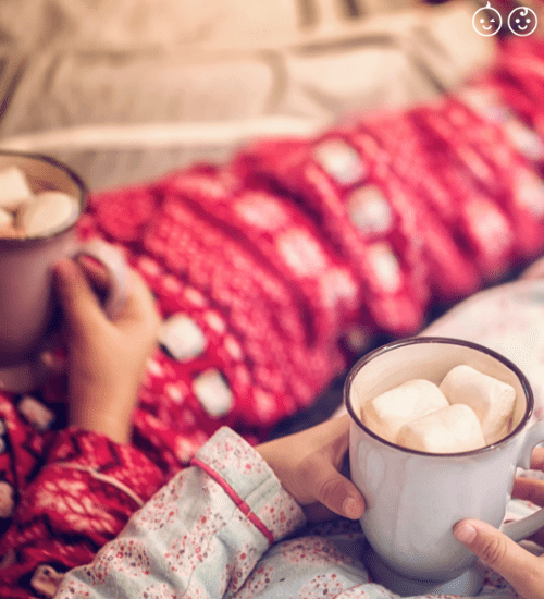 2 kids in holiday season pajamas holding hot chocolate with marshmallows