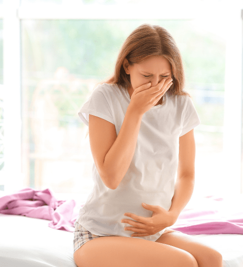 pregnant woman sitting in bed holding her belly and mouth form morning sickness