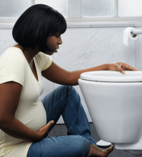 pregnant woman sitting on the floor in front of a toilet from morning sickness