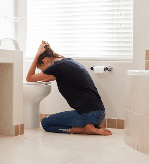 woman leaning over toilet, sitting on the bathroom floor from morning sickness
