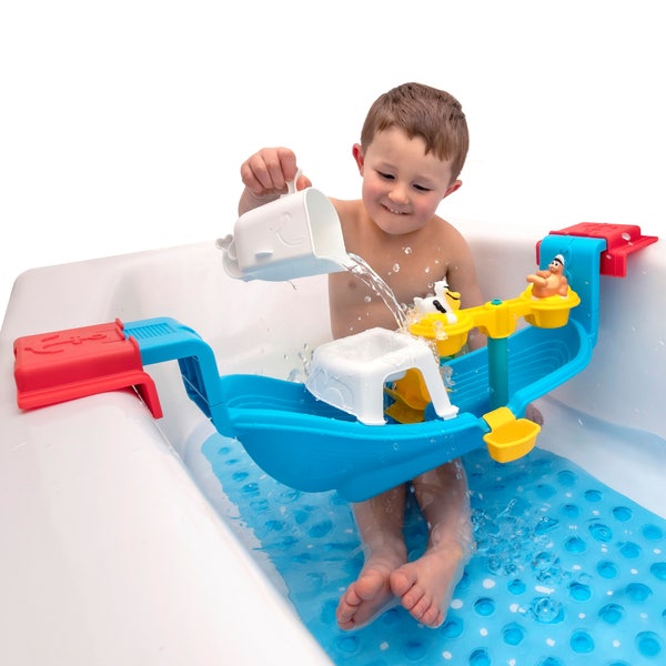 Toddler boy sitting in the bathtub, pouring water in a kids' bath caddy with blue, red, and yellow pieces attached.