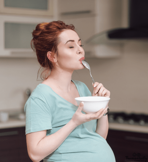 a pregnant woman eating off a spoon while holding a bowl after dysgeusia