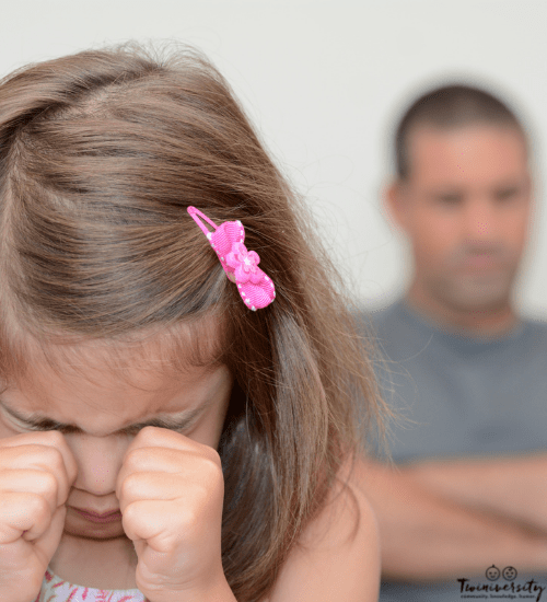 little girl crying in her hands and Dad watching behind her