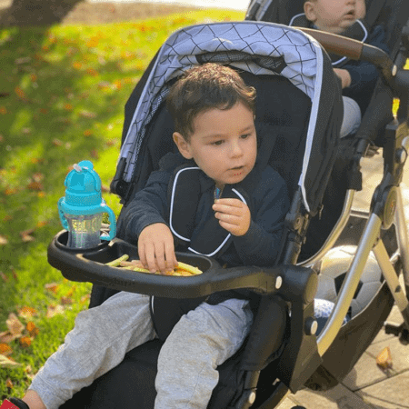 2 kids in a tandem stroller with a snack tray