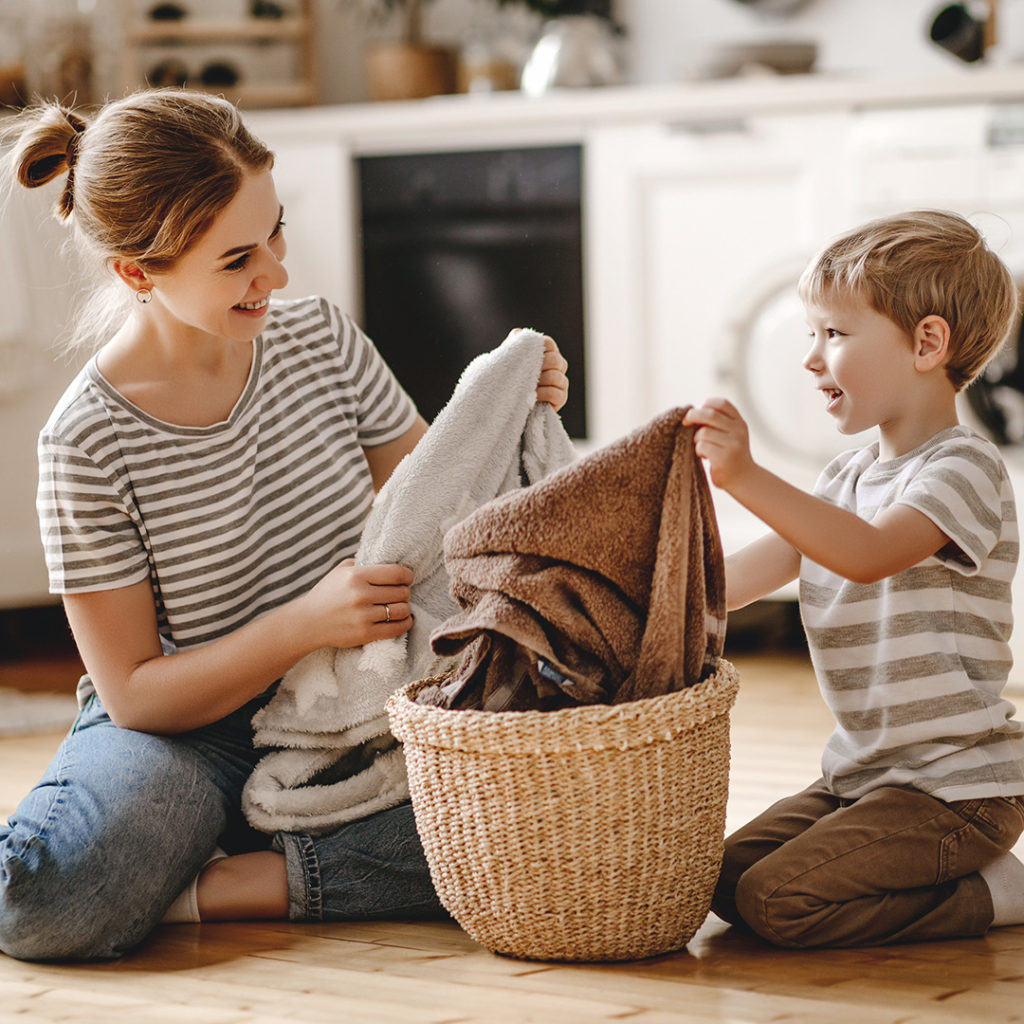 Happy mother and son sitting on the floor in the laundry room folding bath towels together