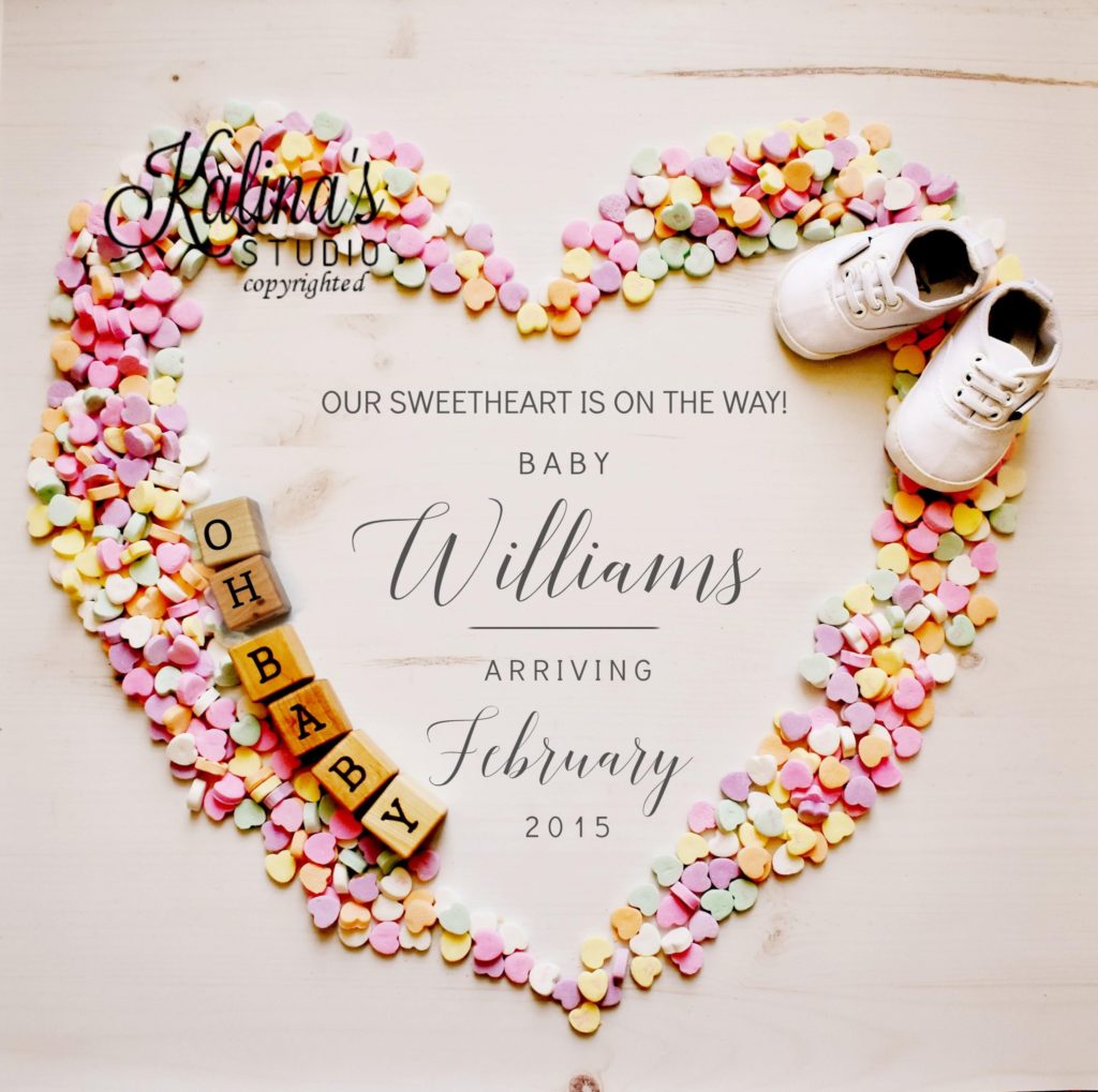 Pregnancy announcement with gray text, "Our Sweetheart is on the Way! Baby Williams arriving February 2015," surrounded by multicolored conversation hearts in the shape of a heart, wooden blocks reading "OH BABY," and a pair of white baby shoes.