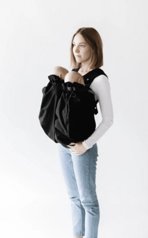 a woman holding two infants in a front carrier for twins