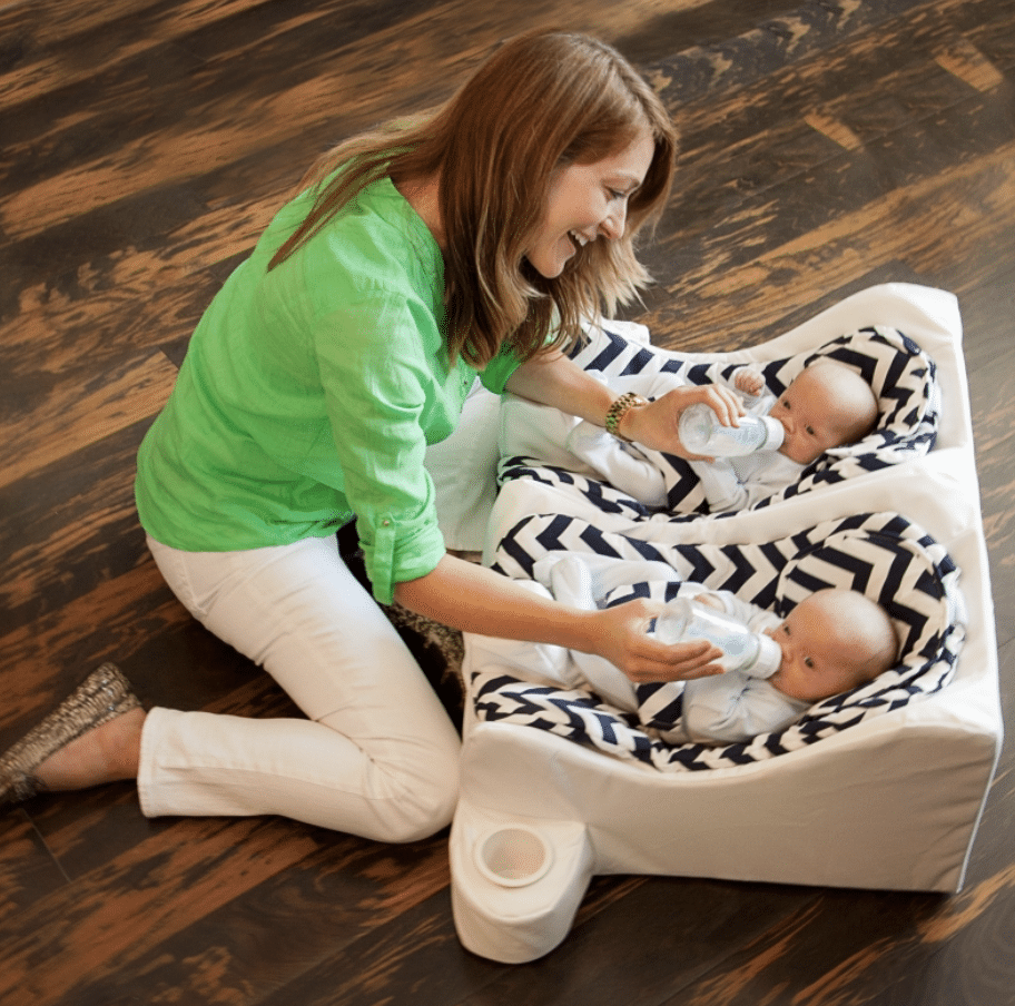a woman sitting on the floor bottle-feeding infants twins in a table for two seat