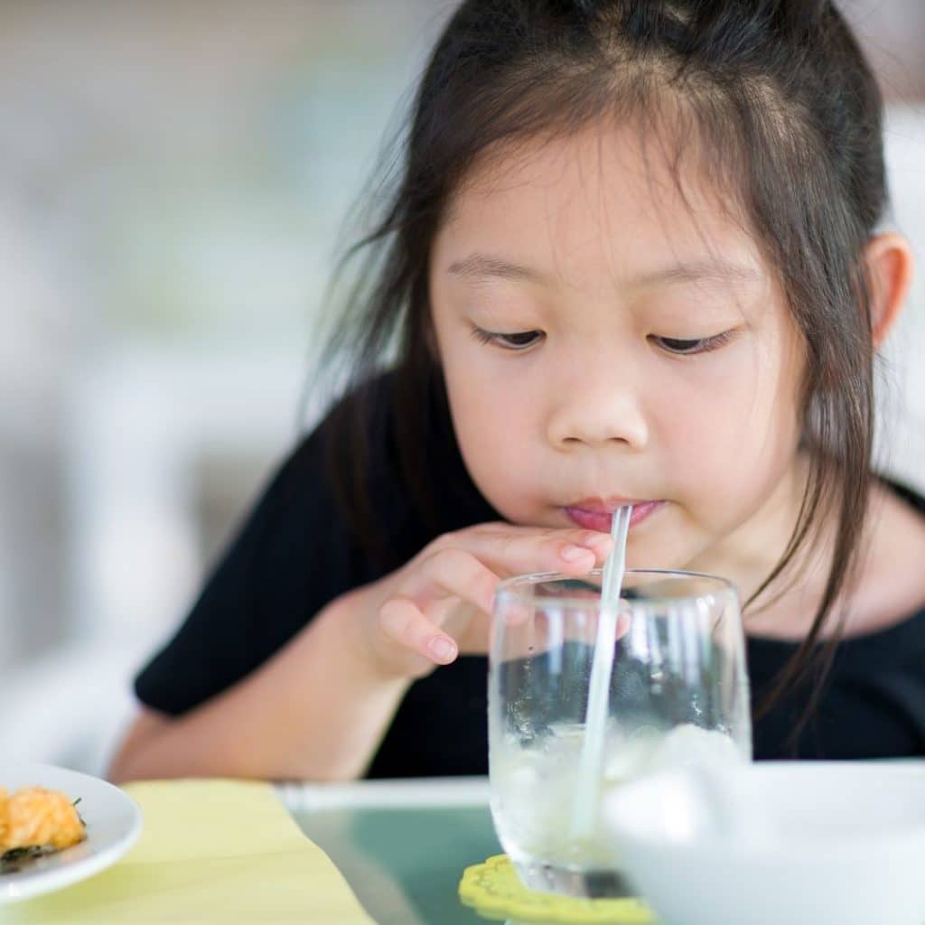 little girl drinking water from a straw in her glass of ice water with her dinner. 