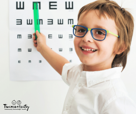 young boy wearing glasses smiling in front of eye exam chart