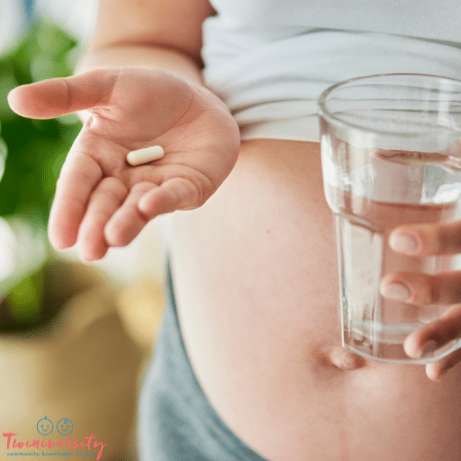 A pregnant lady is holding a pill in her right hand and a glass of water in her left hand. She has her shirt pulled up allowing her pregnant belly to show.