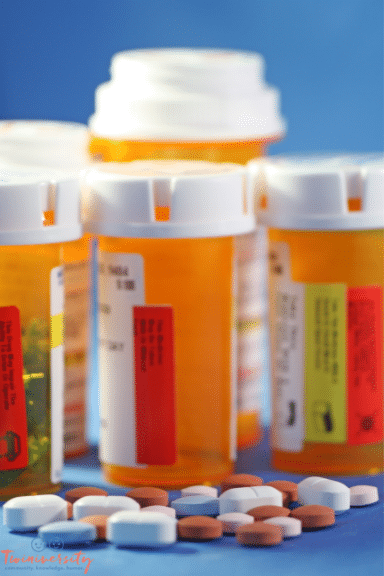 4 prescription pill bottles are blurred in the background, with a variety of pills scattered in the foreground.
