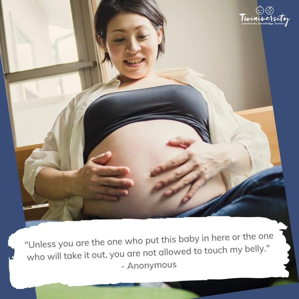 Very pregnant woman is sitting cross-legged on a bench, t-shirt pulled up, exposing her pregnant belly with both hands resting on her baby bump. She is smiling and looking at her pregnant belly