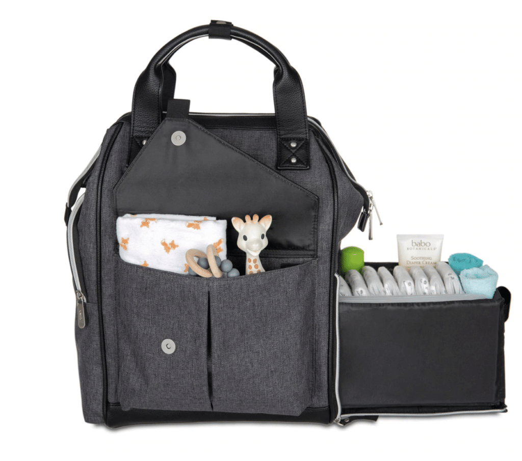 a dark grey diaper bag with a small giraffe and a folded burp cloth in an open pocket. a slide out caddy with diapers and lotion in it