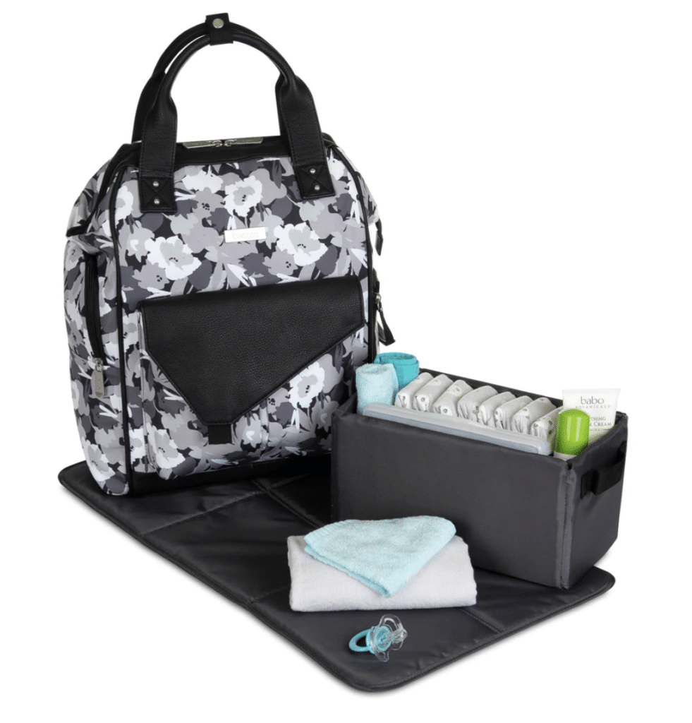 a black, white, and grey floral patterned diaper bag with a changing pad and caddy full of diapers and lotions and burp cloths.