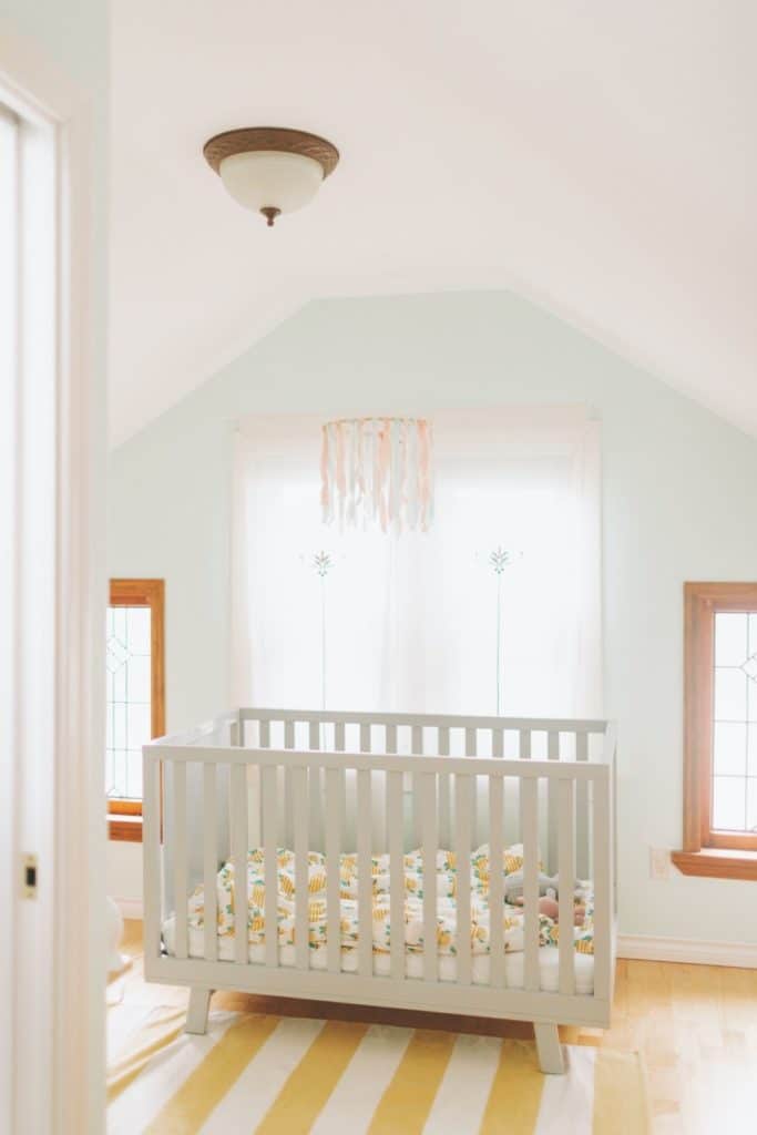 White crib in nursery with mint green walls and windows on each side of the crib. 