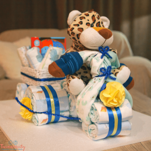 diapers rolled up and connected with ribbon and a stuffed tiger on top sitting on a table 