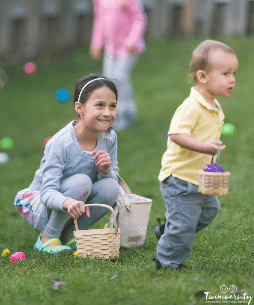 a young girl crouched down holding a basket and a boy running away with another basket in the grass during a easter egg hunt outside