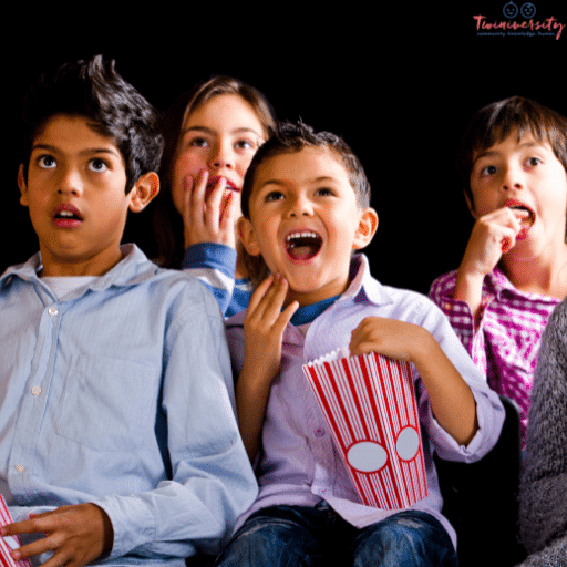 4 young kids watching a screen eating popcorn