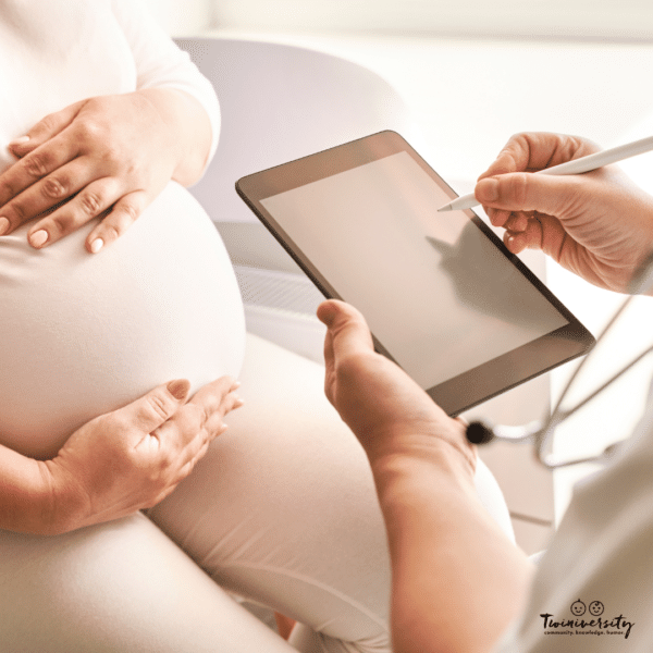 pregnant woman holds her abdomen while a doctor takes notes for prenatal genetic testing