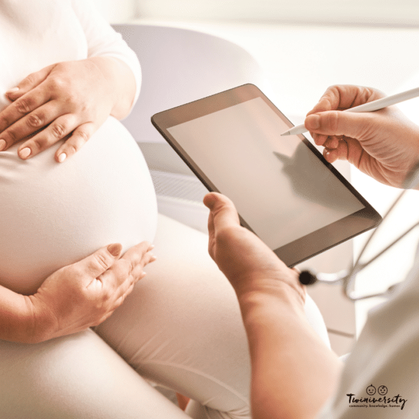 pregnant woman holds her abdomen while a doctor takes notes for prenatal genetic testing
