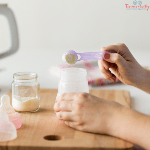 a hand holding a baby bottle and the other hand scooping formula into it on a wooden cutting board