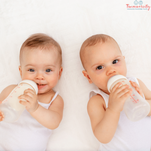 infant twins in white tank tops on a white background holding baby bottles