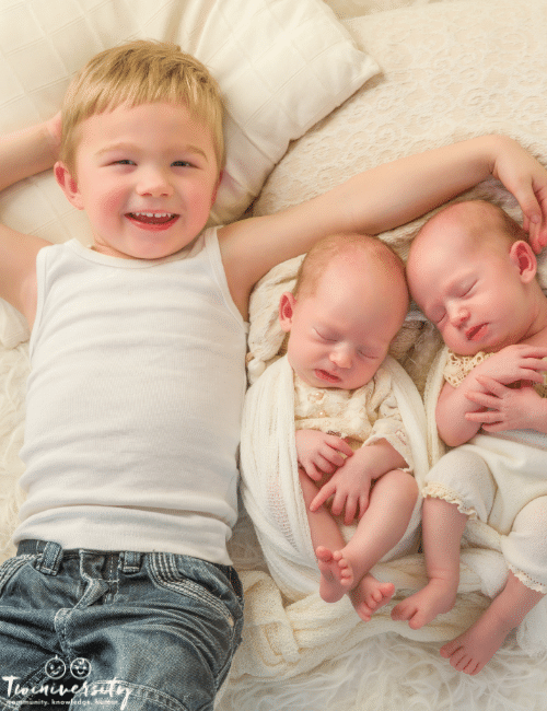 infant twins and older sibling boy with his arm over them