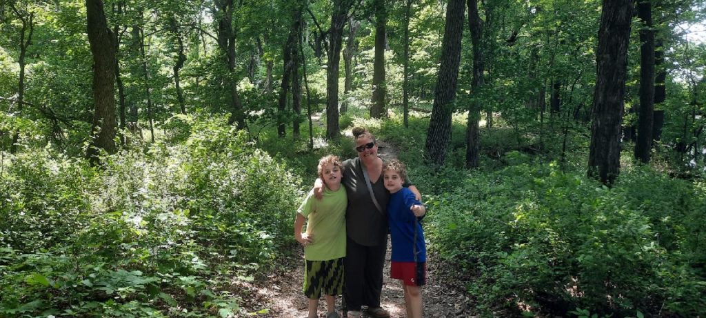 a woman with twin boys on either side standing on a path in a forest for Mother's Day