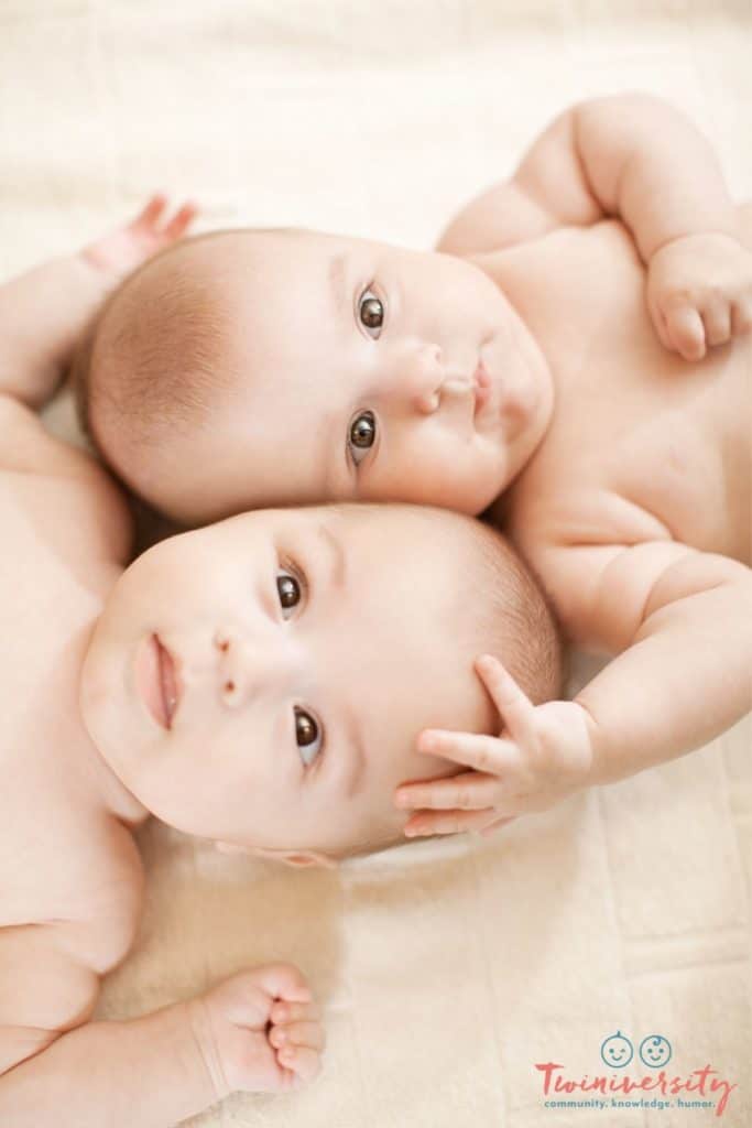 Baby twins lying head to head, looking straight into the camera.