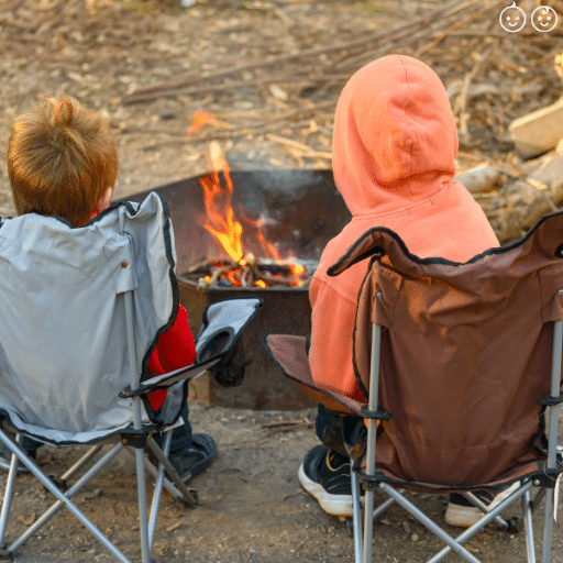 the back of two children sitting in camping chairs in front of a camp fire outside