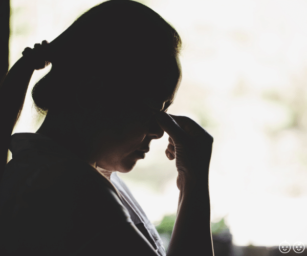 A woman in profile with a pony tail pinching the bridge of her nose with her fingers.