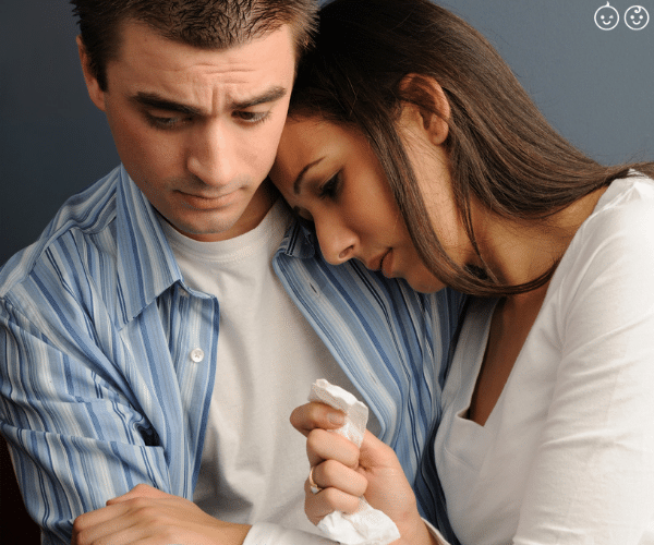 a man comforting a woman holding a tissue in grief over a miscarriage