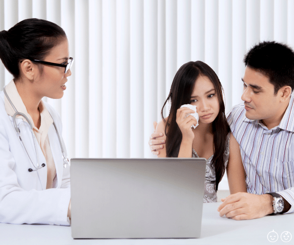 a doctor showing a couple a computer screen.  the man has his arm around the woman who is holding a tissue, grieving her miscarriages