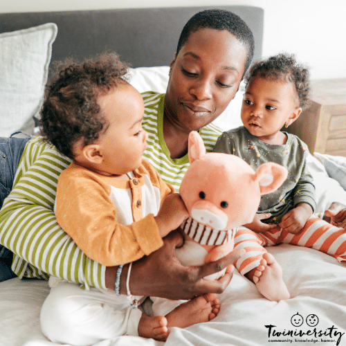 A mom manages her twins solo while playing with them on a bed
