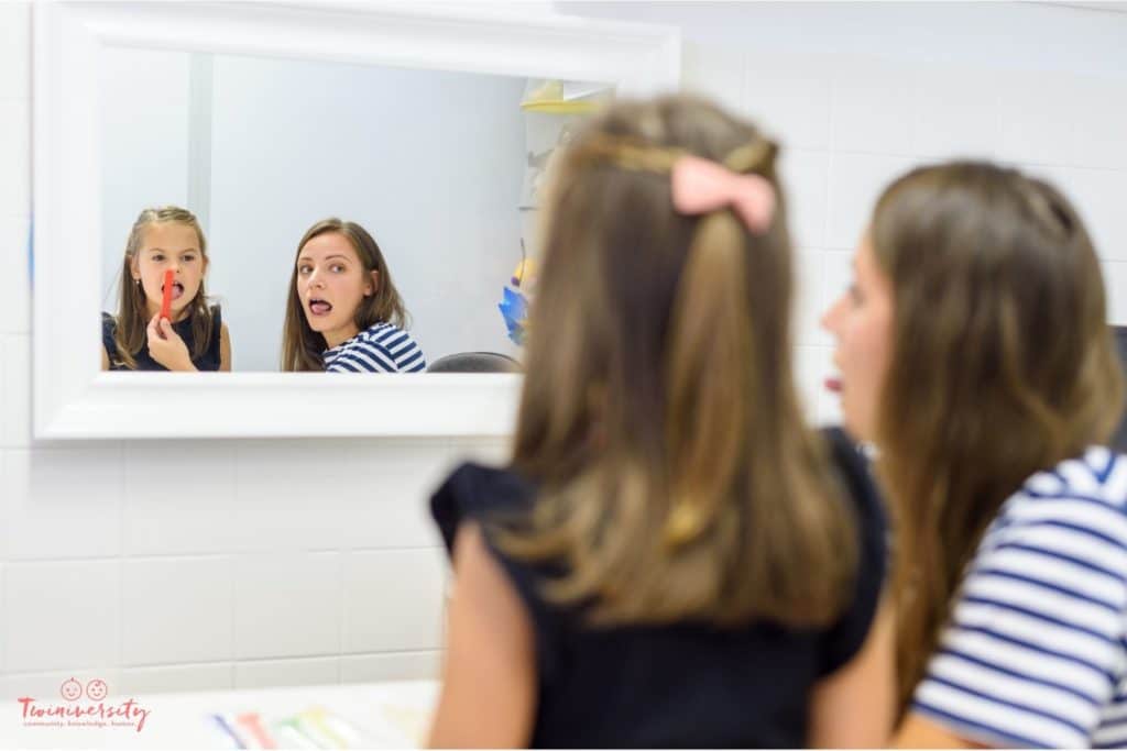 Little girl is working with a speech specialist. They are practicing in a mirror.
