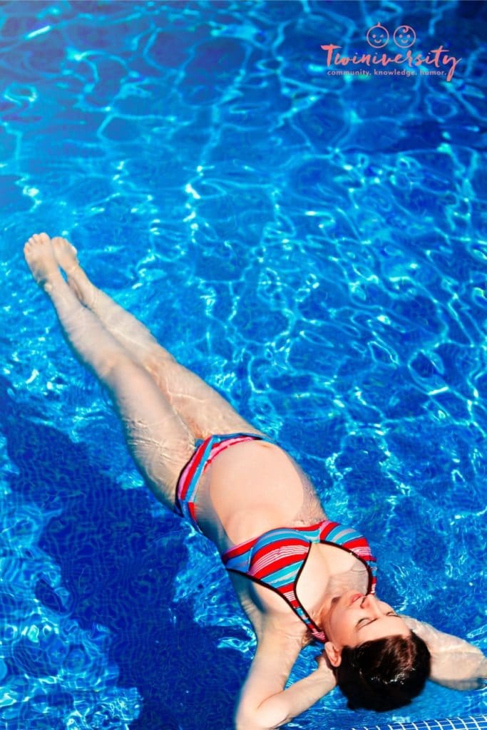 Pregnant woman floating on her back in a swimming pool while wearing a red and blue striped bikini