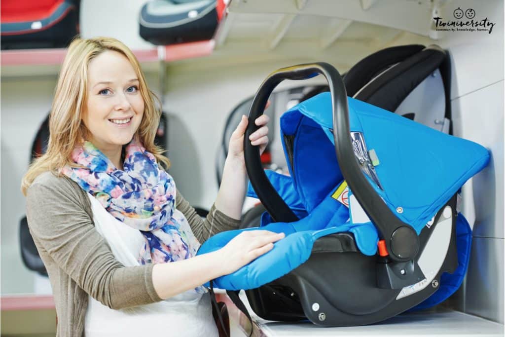 A pregnant woman shopping for an infant car seat. She is currently looking at a blue and black infant carrier car seat. 