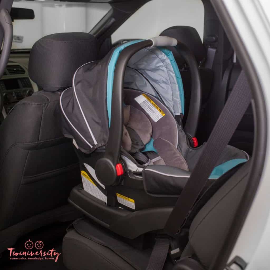 An empty infant car seat is installed in the backseat of a car, behind the drivers side and touching the back of the rear seat, meaning this car seat does not fit properly in this car.