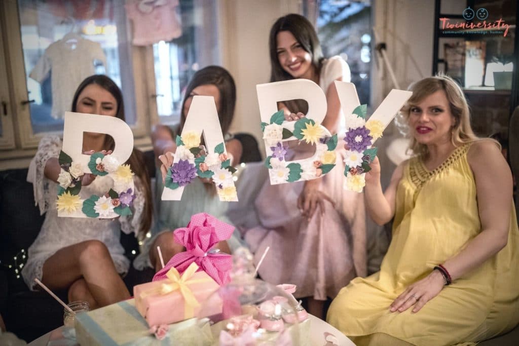 Four women hold up white letters with flowers on them to spell out BABY.