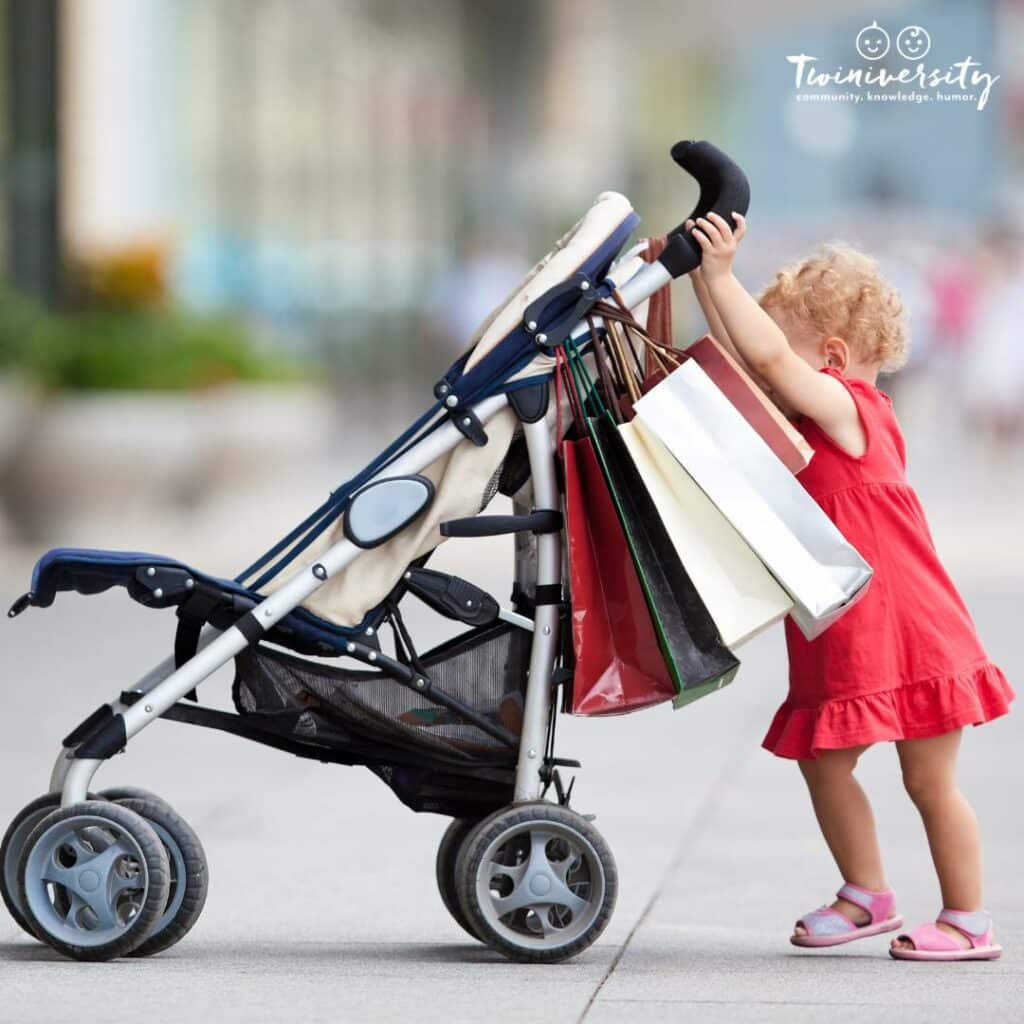 Toddler pushing a stroller with shopping bags hanging from the handles