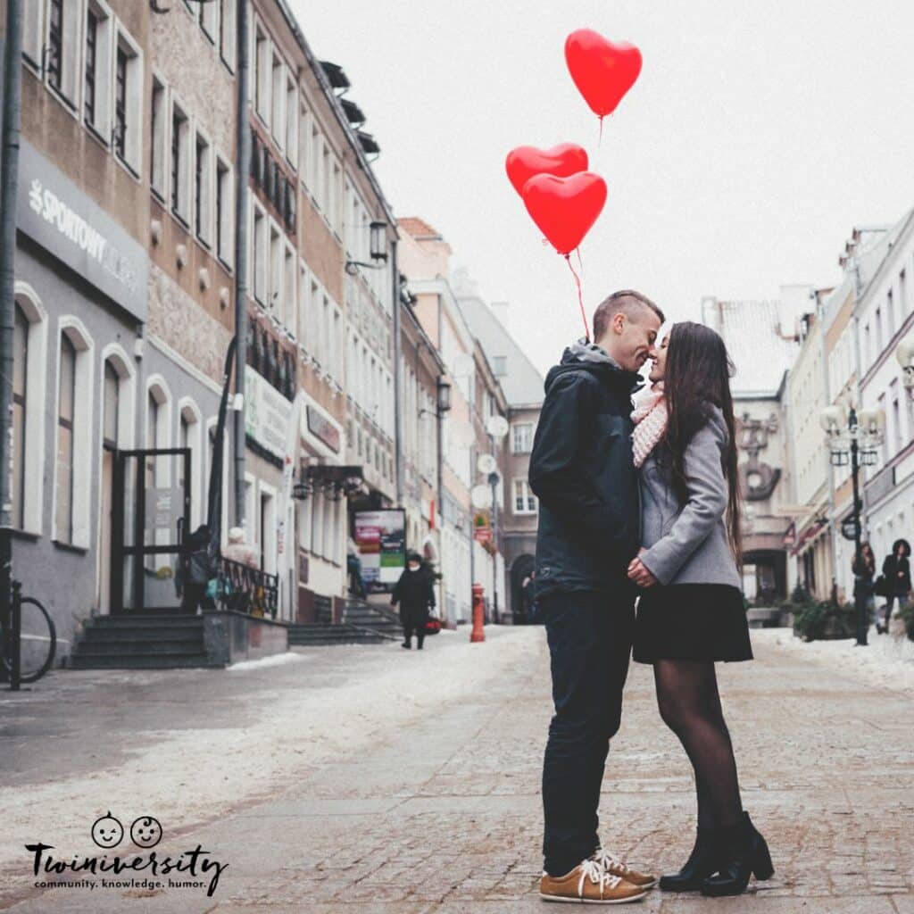 a couple standing in the middle of the street embraced in a hug with heart balloons