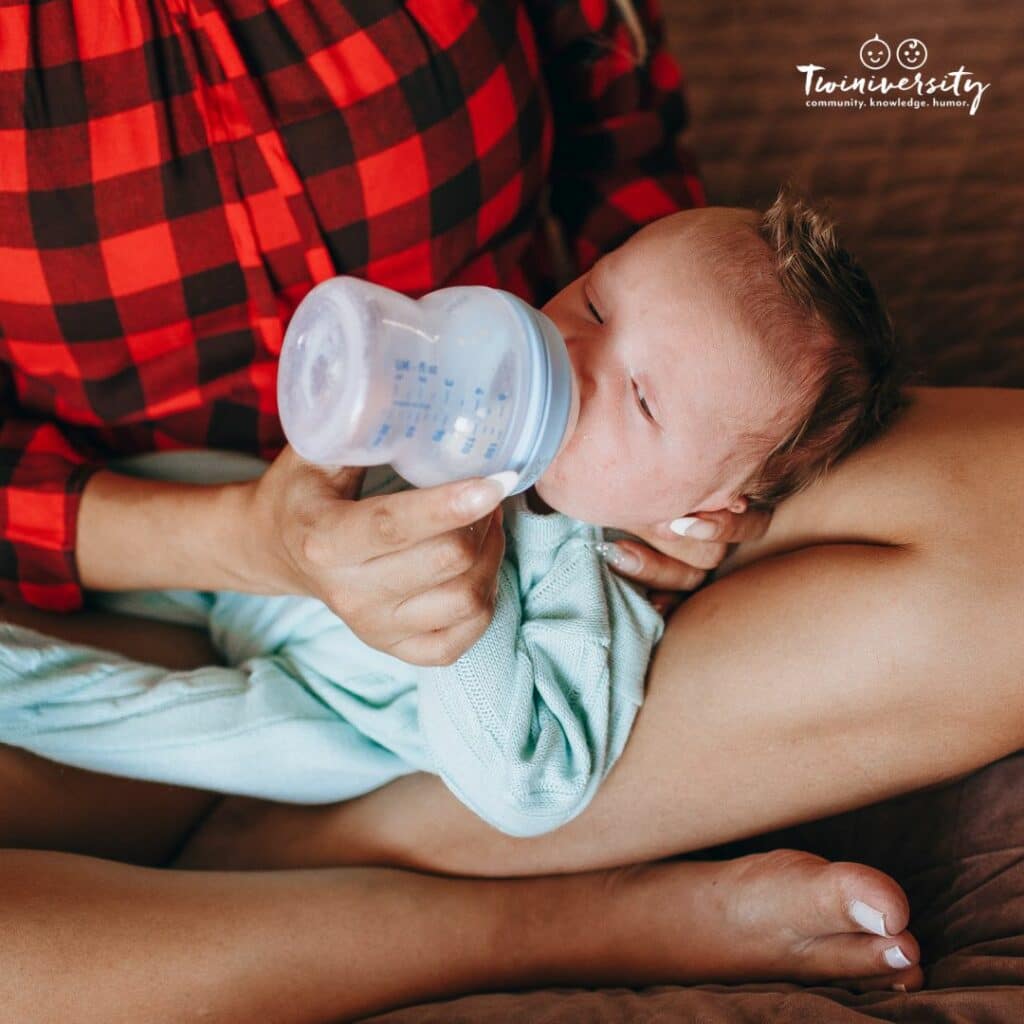 An infant is being held in a cradle position while being fed with a wide shaped bottle