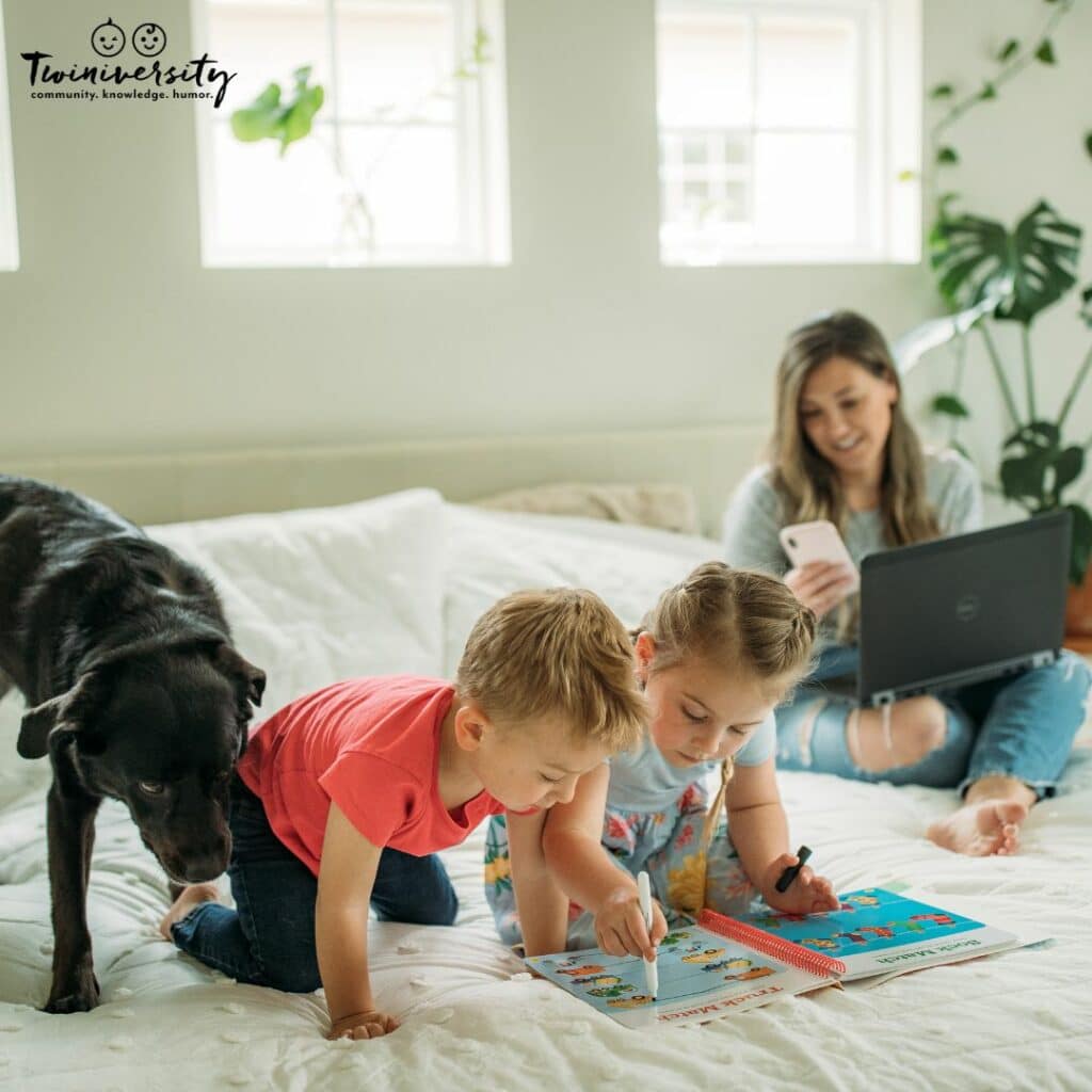 Work from home mom sitting on her bed with her twins coloring 