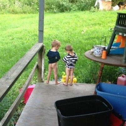 two little boys with no pants, standing on the edge of a porch peeing into the grass at a distance