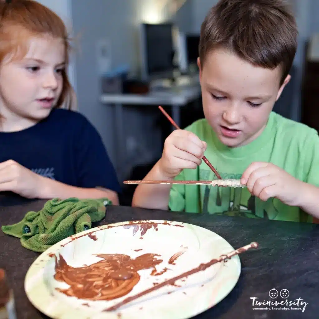 twin girl and boy painting sticks for a fun summer arts and crafts project