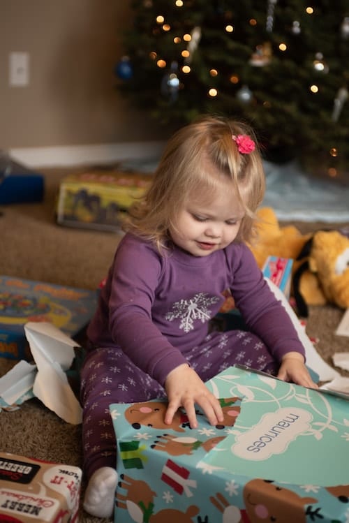 little girl opening presents in front of christmas tree the 4 gift rule