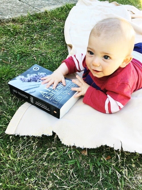 baby holding large book lying on blanket on the grass kids to read